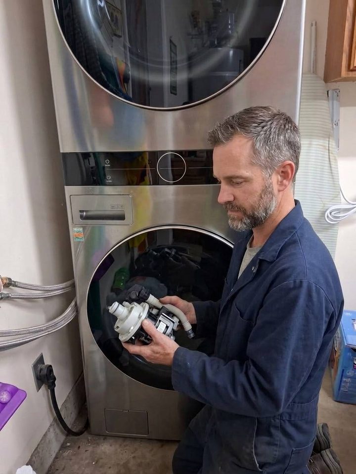 Technician holding a washer drain pump at a stacked laundry pair